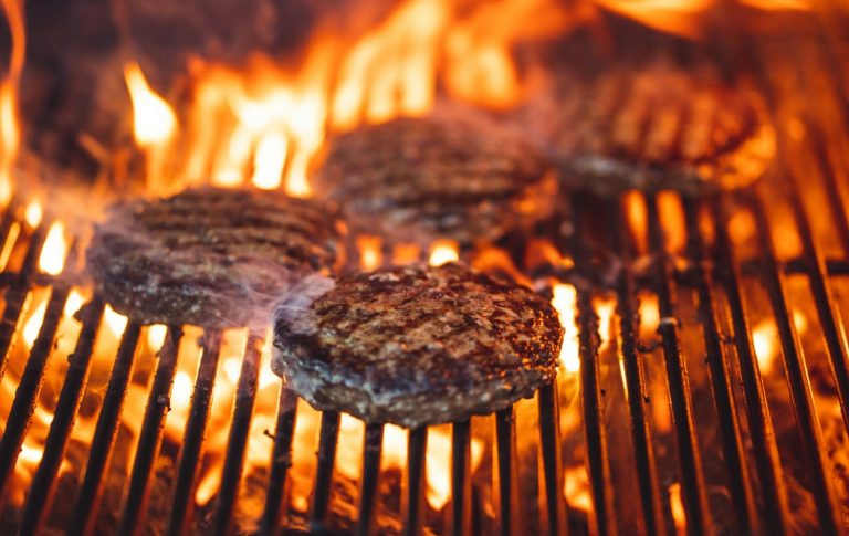 Saftige Burger-Patties brutzeln auf einem Grill über offener Flamme.