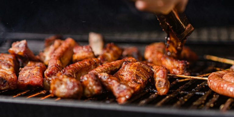 Gegrillte Fleischstücke und Würstchen auf einem Grill, werden mit einer Marinade bestrichen.