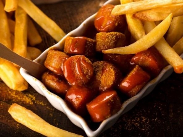 Currywurst mit Sauce und Pommes in einer Schale serviert.