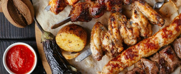 Grillplatte mit verschiedenen Fleischsorten, gegrilltem Gemüse und Dips.